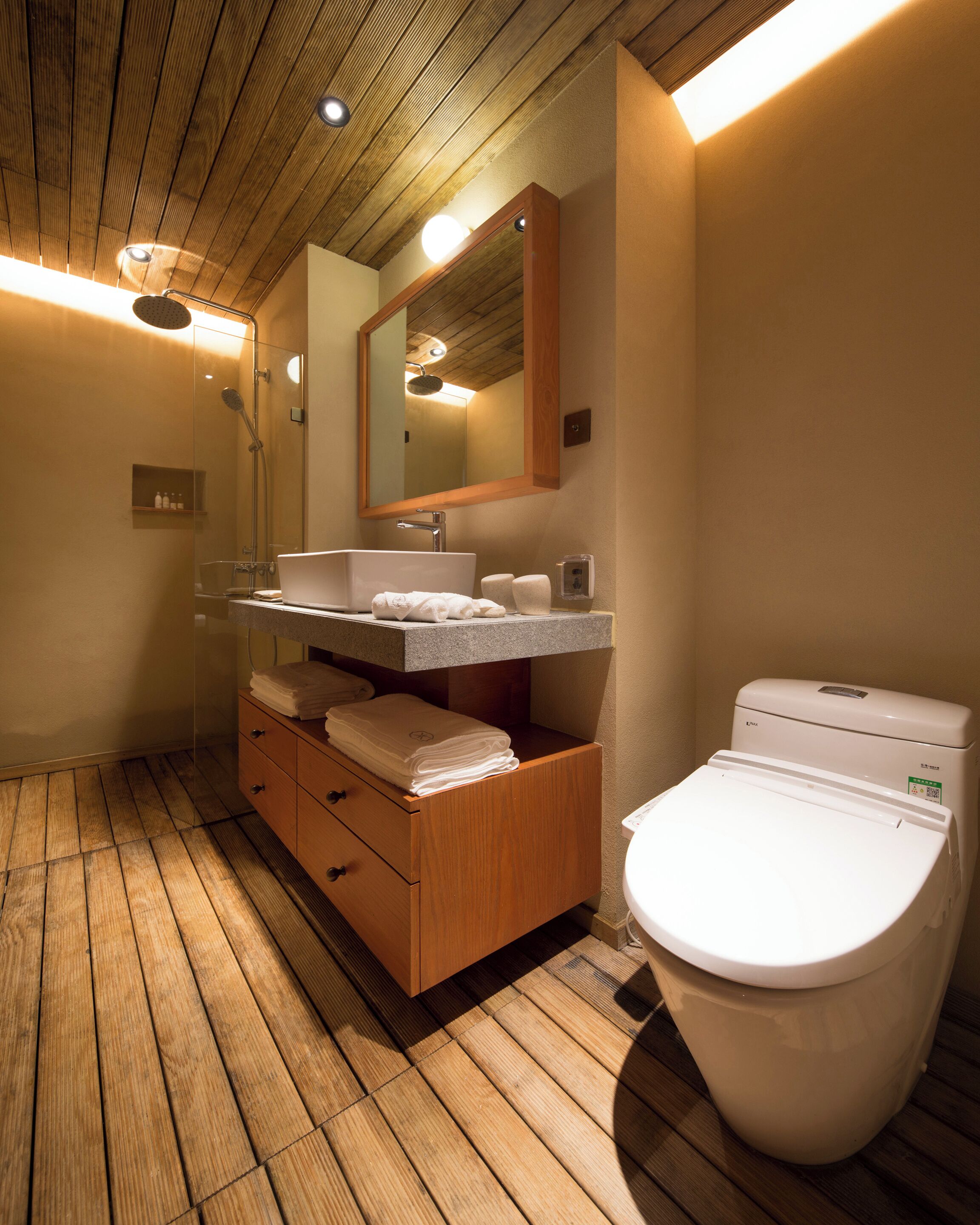 Une salle de bain moderne avec un plancher en bois, un lavabo surmonté d’un miroir et des toilettes.