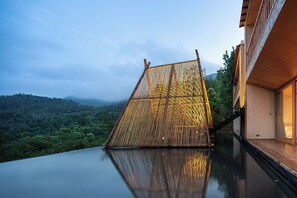 Relax by the serene pool surrounded by lush greenery and a sleek, modern structure.