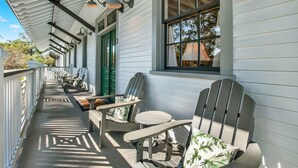 Un porche cubierto con sillas Adirondack y un banco, revestimiento blanco y una puerta verde.