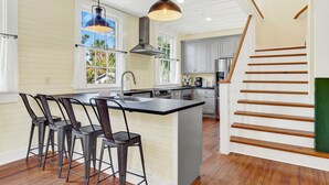Una cocina con una isla central, taburetes de bar, una lámpara colgante y una escalera de madera.