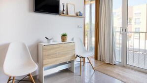 Een moderne woonkamer met een flatscreen televisie, een houten kast, twee witte stoelen en een schuifdeur naar een buitenbalkon.