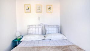 Een slaapkamer met een bed, twee kussens, een nachtkastje met een lamp en drie ingelijste foto's aan de muur.