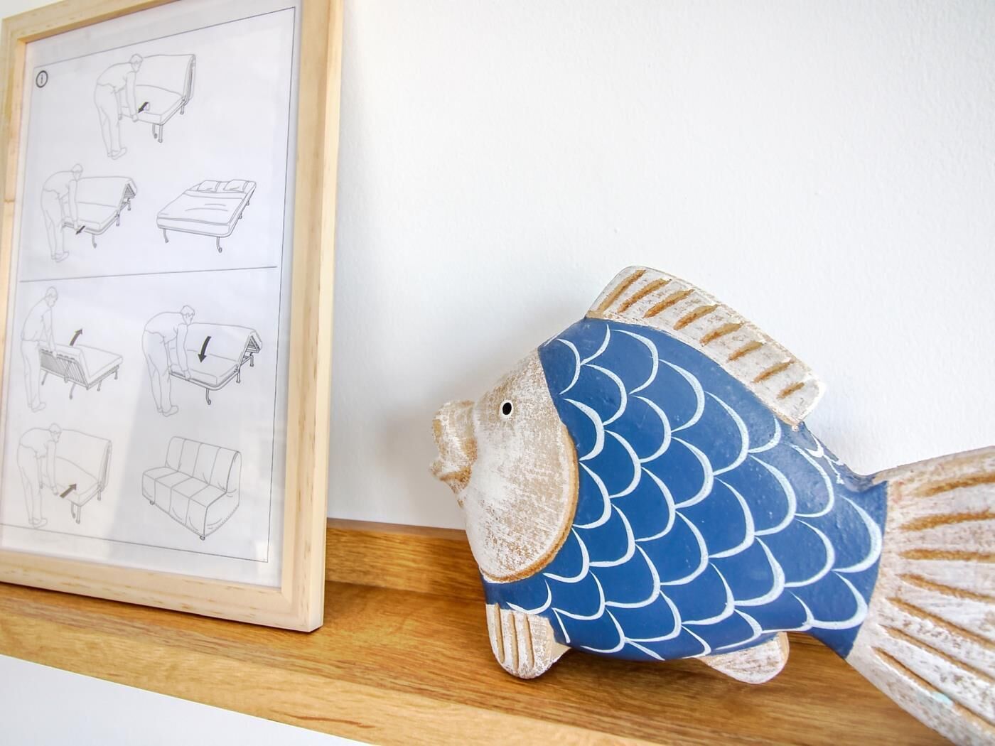 A fish-shaped object with a blue and white pattern, a framed diagram with illustrations of furniture assembly, and a wooden surface.