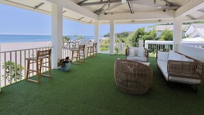 Un espace extérieur abrité, doté d’un revêtement de gazon synthétique, de chaises en bois, de meubles en osier et offrant une vue sur la plage.