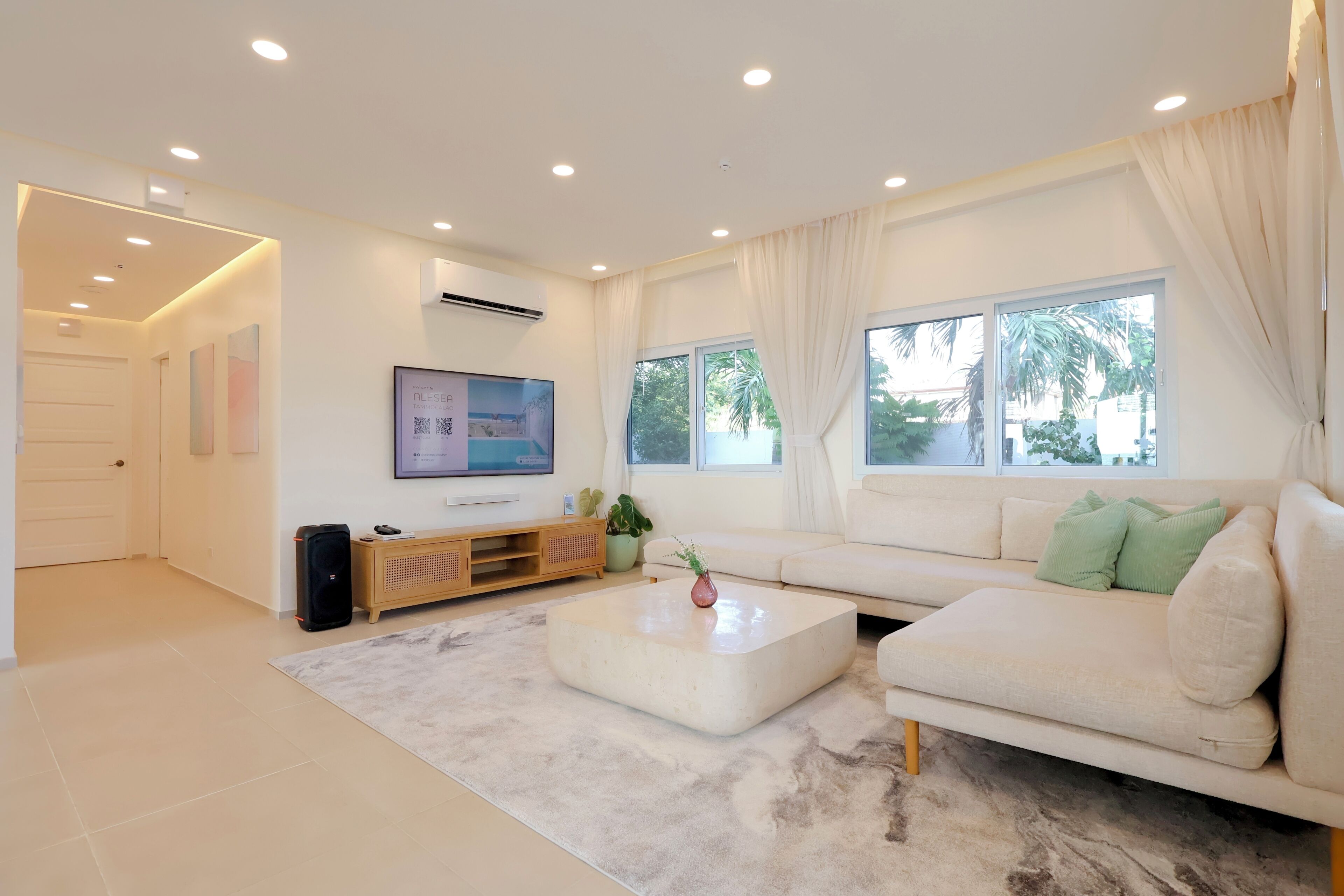 A modern living room with a sofa, coffee table, TV, and a large window with curtains.
