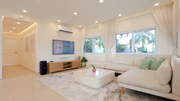 A modern living room with a sofa, coffee table, TV, and a large window with curtains.