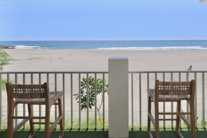 Two wicker chairs facing a beach with a view of the ocean.
