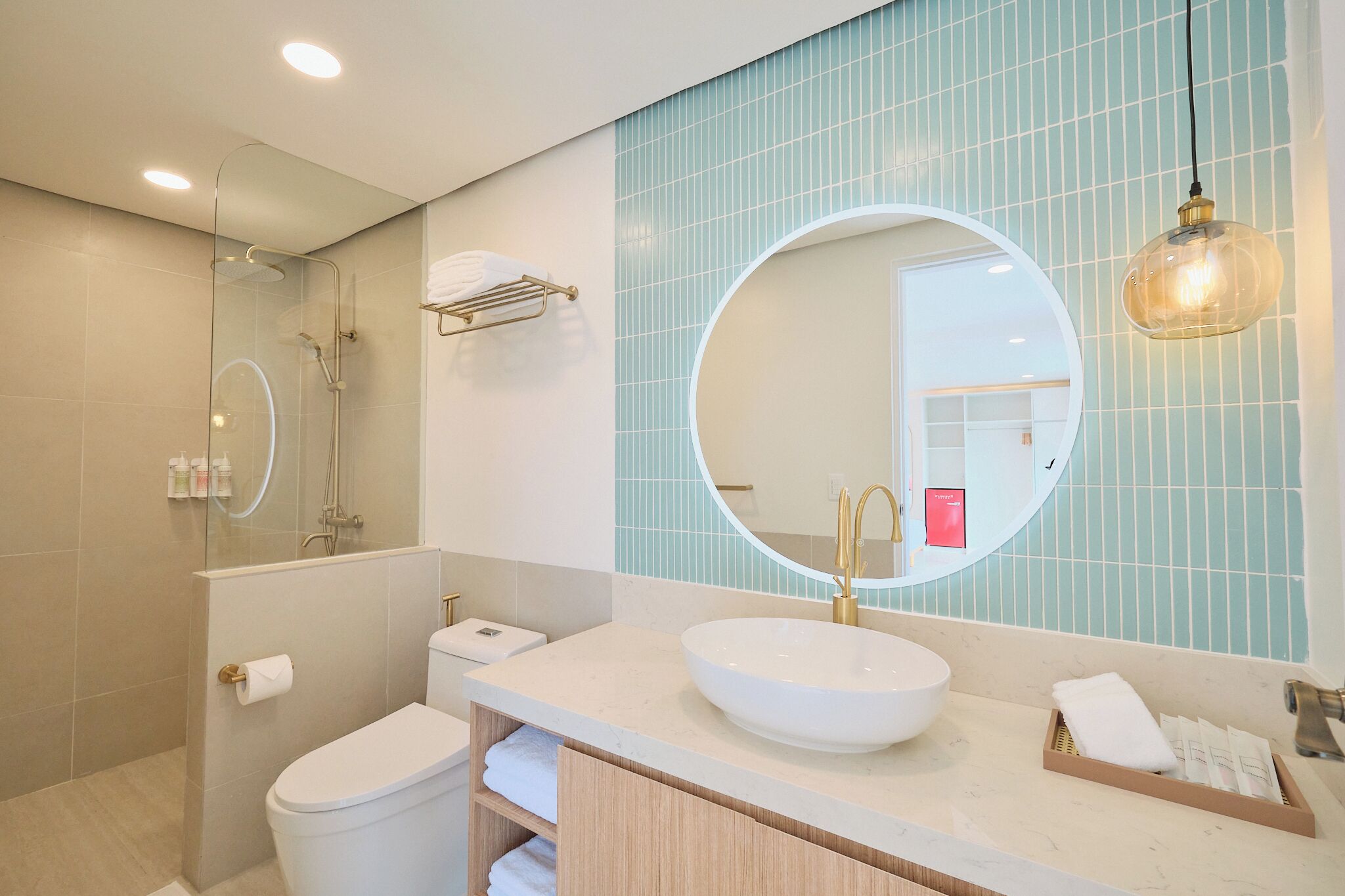 A modern bathroom with a glass-enclosed shower, a round mirror, and a white sink.