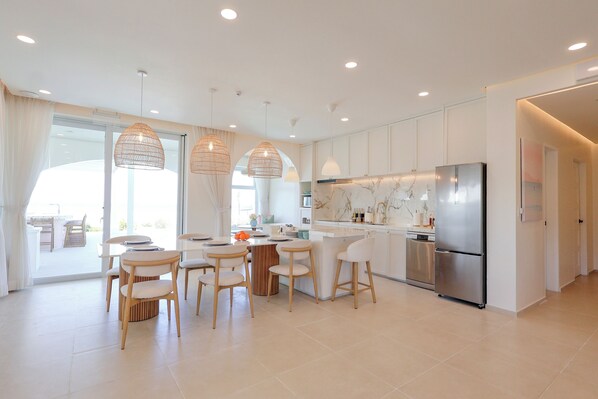 A modern kitchen with white cabinetry, a stainless steel refrigerator, and pendant lighting.