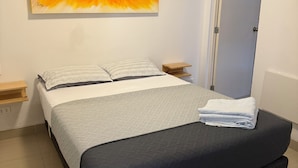 A bedroom with a bed, a painting on the wall, a door, and a small wooden nightstand. - SGH Paracas (Paracas)