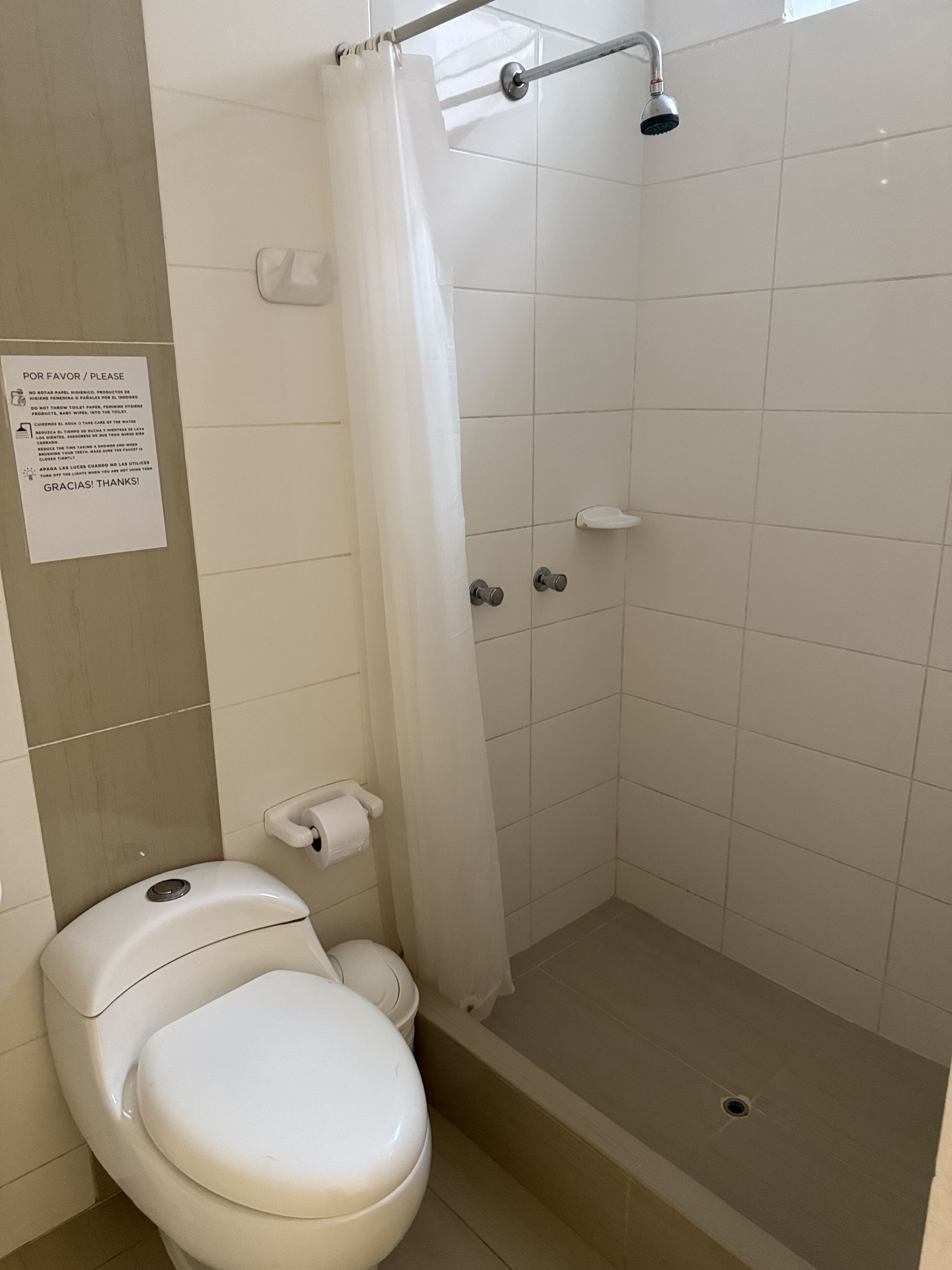 A bathroom with a toilet, shower, and a sign on the wall.