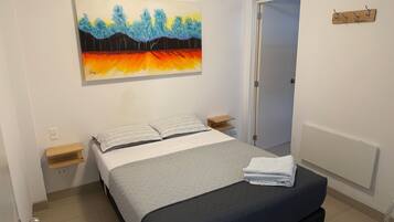 A bedroom with a bed, a painting, a door, and a wall-mounted shelf.