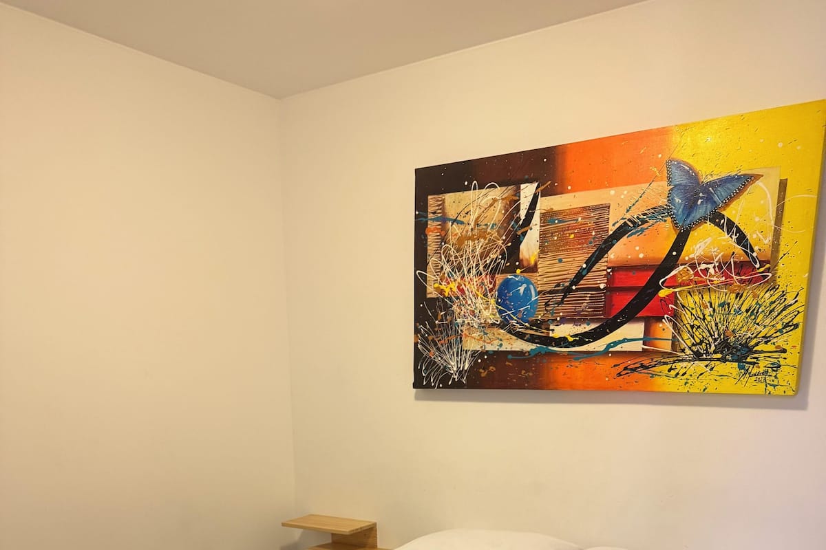 A neatly made bed with a geometric patterned bedspread, a quilted pillow, and two folded towels with orange tags.