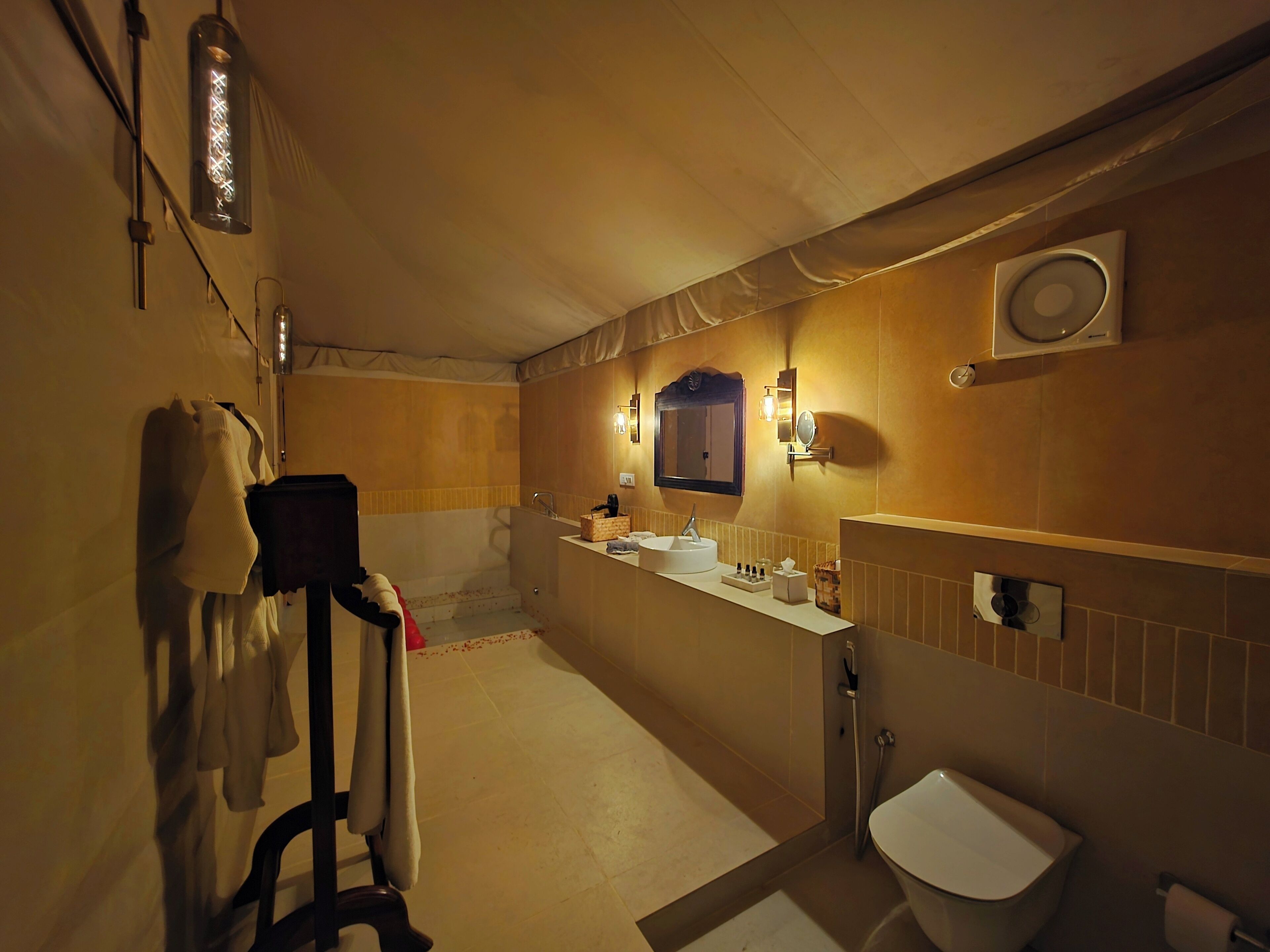 A bathroom with a shower, sink, and toilet. There are towels hanging on a rack, a mirror, and a wall-mounted light fixture.
