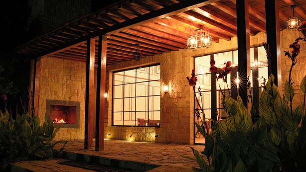 A stone-floored patio with a fire feature, wooden beams, and large windows.