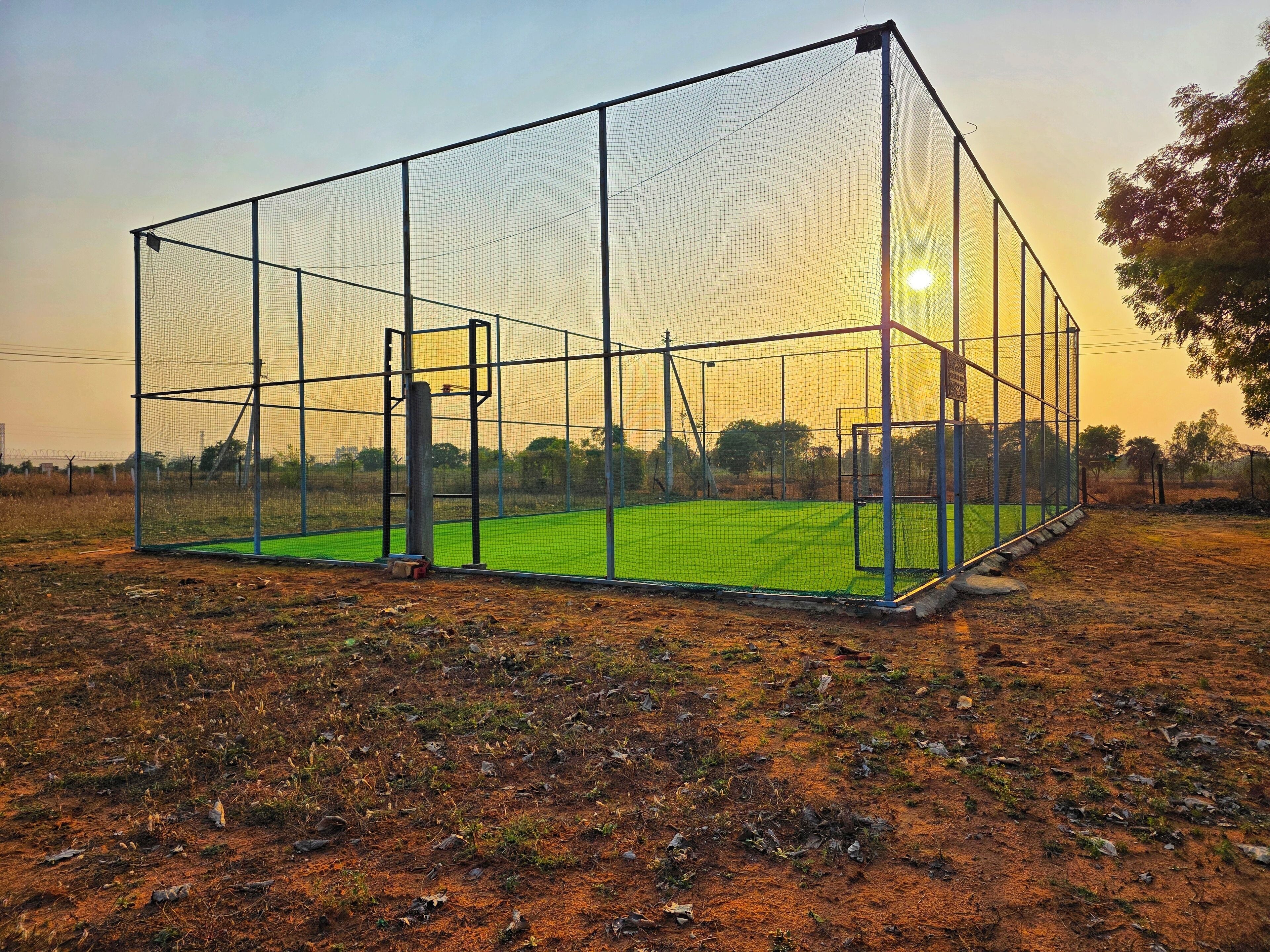 A sports court with a netted enclosure and a basketball hoop.