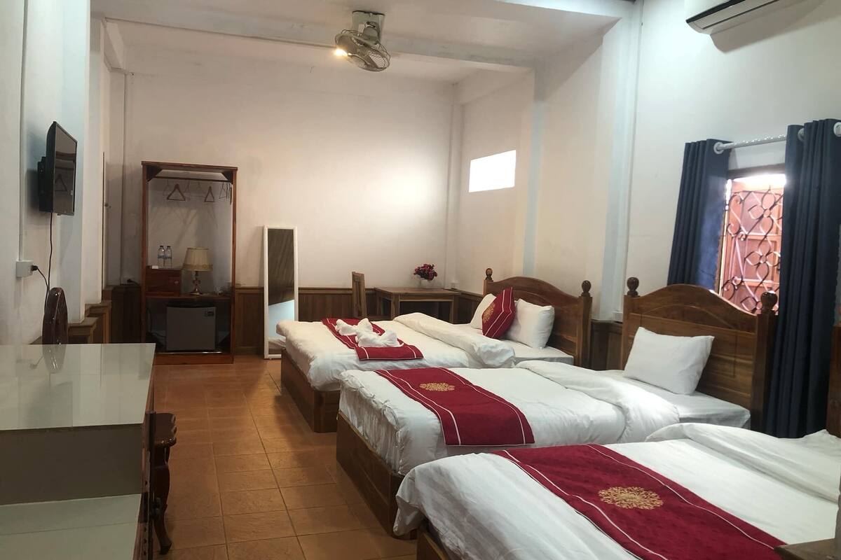 A hotel room with four single beds, a desk, a chair, a TV, a wardrobe, and a mirror.