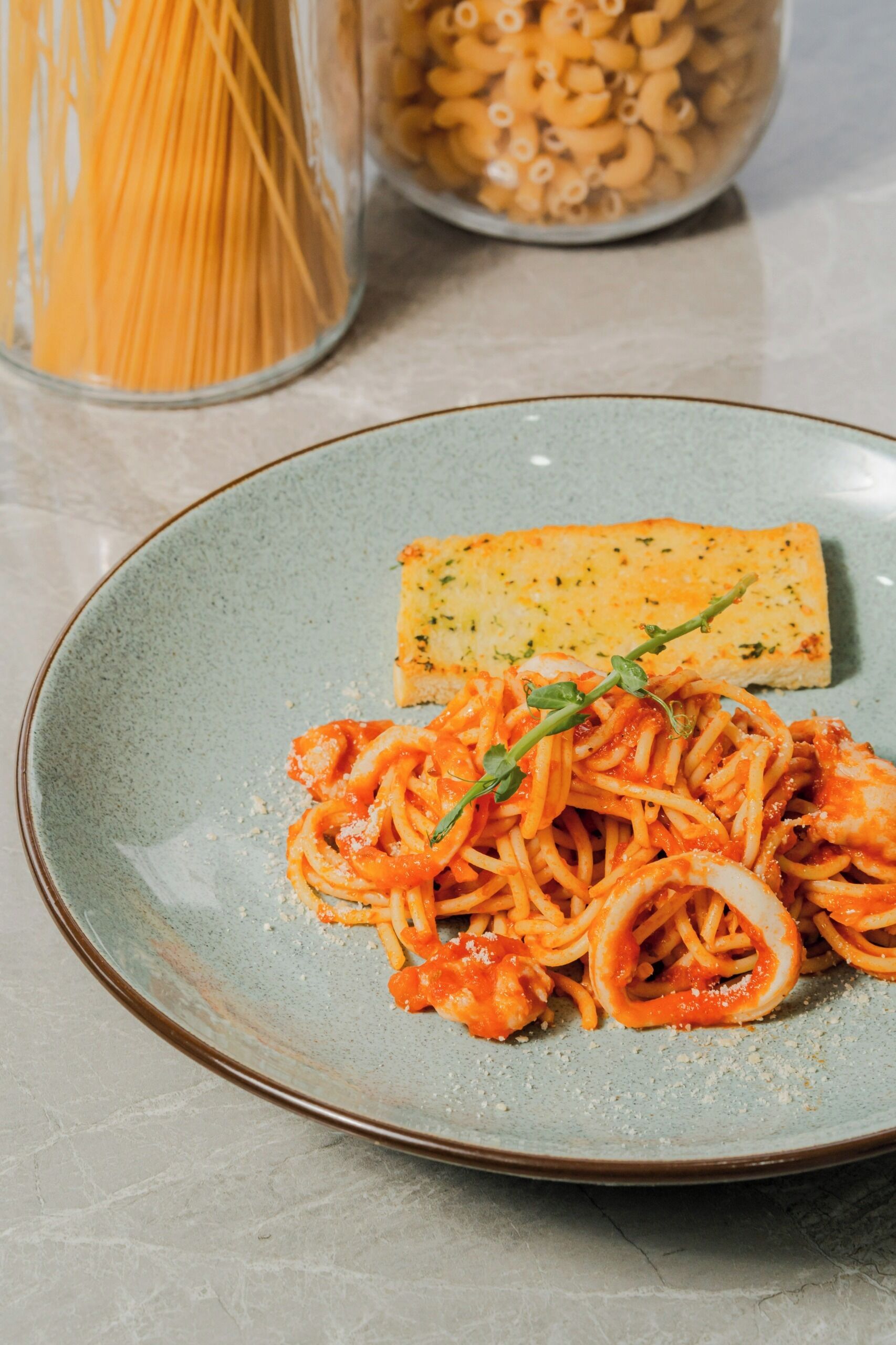 A plate of spaghetti with a slice of bread and a garnish on a ceramic plate.