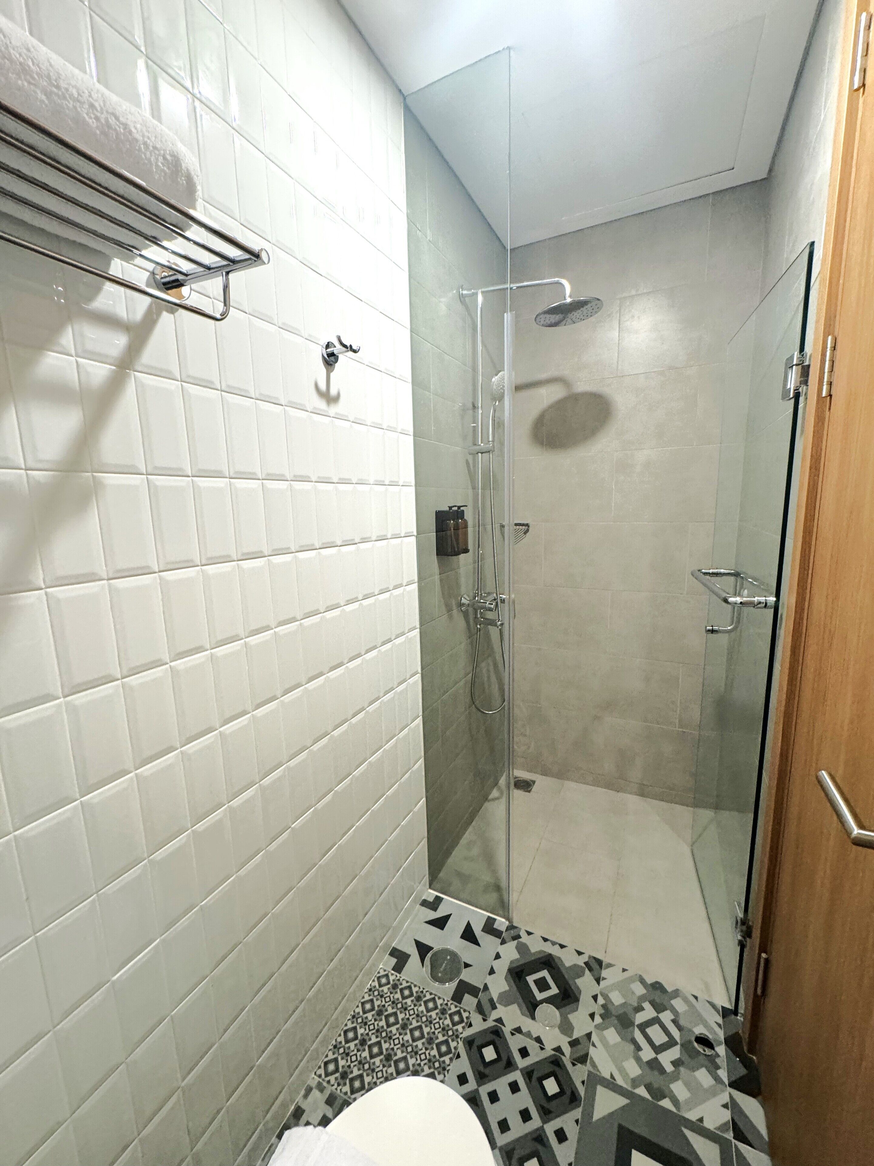 Un baño pequeño y moderno con paredes de azulejos blancos, una ducha con puerta de cristal y piso estampado.