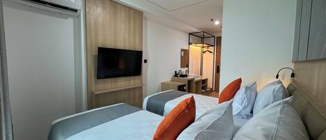 A hotel room with two beds, a TV mounted on the wall, a mirror, and a small bathroom area.