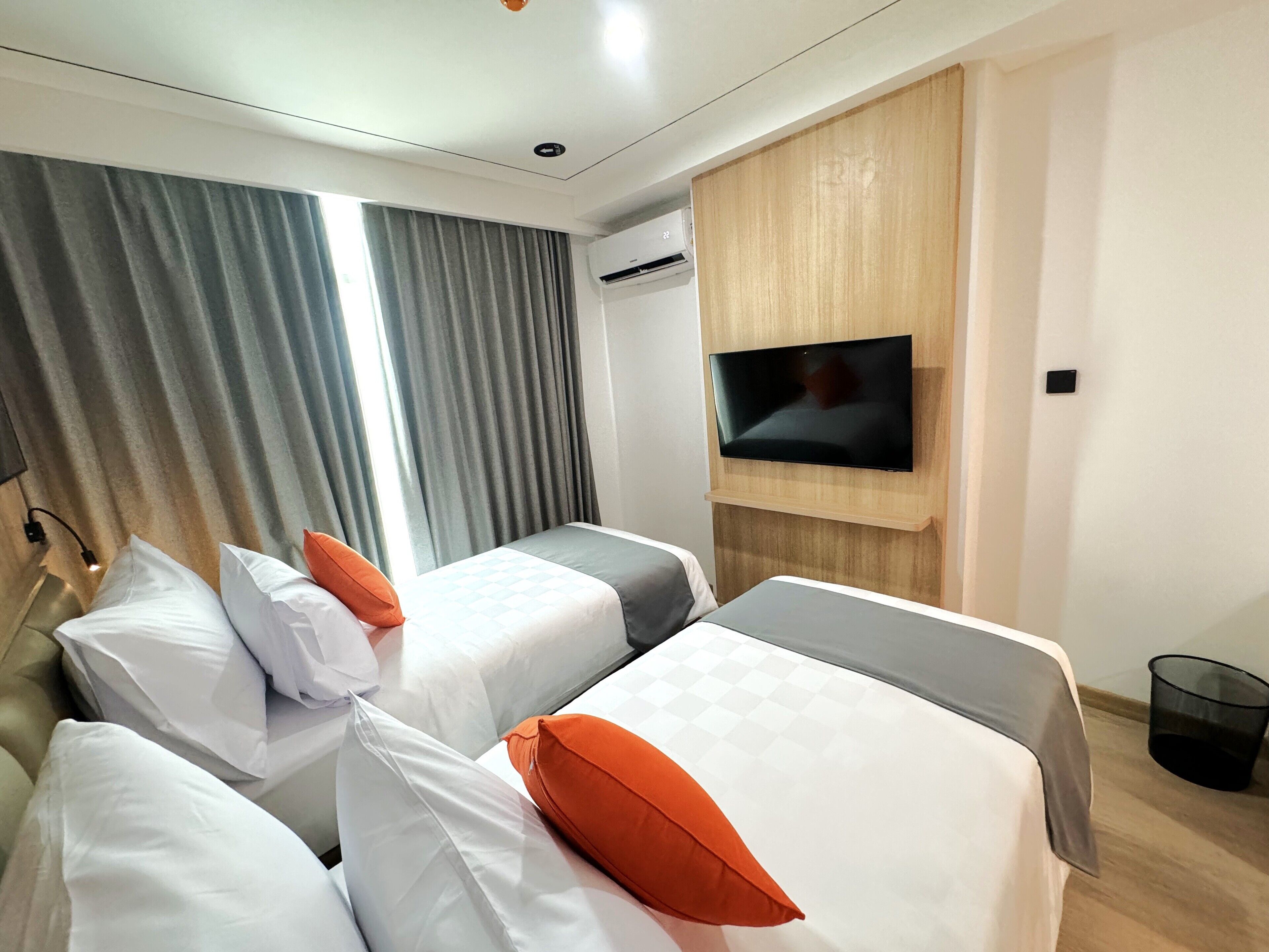 A hotel room with two beds, a TV mounted on the wall, and a window with curtains.