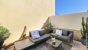 Un espace extérieur aménagé avec un canapé et une table, entouré de plantes et d’un cactus.