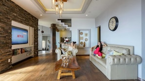 Een moderne woonkamer met een flatscreen televisie, een houten salontafel, een beige bank en een trap die naar een hoger niveau leidt.