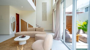 A modern living room with a sectional sofa, a small coffee table, and a large window with curtains. - Lyma Loft (Munggu)