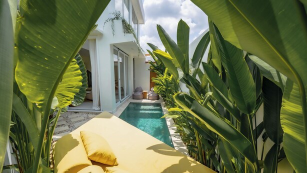 A poolside area with a yellow lounge chair, surrounded by large green plants. - Lyma Loft (Munggu)