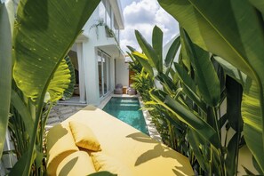 A poolside area with a yellow lounge chair, surrounded by large green plants. - Lyma Loft (Munggu)