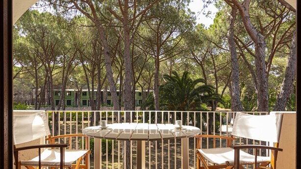 A balcony with a table and chairs, surrounded by trees and a view of a building with green shutters. - Alessia, three-room apartment in Marina di Campo 250 meters from the beach, with air conditioning, p (Marina di Campo)