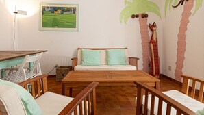 A room with a wooden table, two chairs, a sofa with teal cushions, and a wall mural of a palm tree and a gecko. - Alessia, three-room apartment in Marina di Campo 250 meters from the beach, with air conditioning, p (Marina di Campo)
