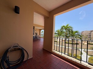 A balcony with a view of palm trees and a building in the background. - Crescent Beach Apt | Ocean View (Palmas del Mar)