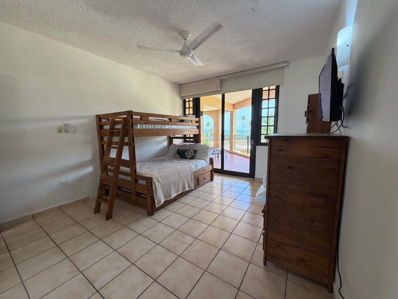 A bedroom with a bunk bed, a wooden wardrobe, a ceiling fan, and a television.