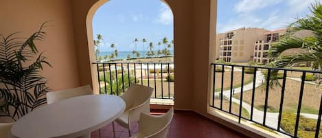 A balcony with a table and chairs, overlooking a pool and palm trees.