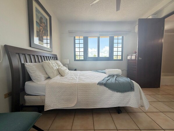 A bedroom with a bed, a window, and a door. - Crescent Beach Apt | Ocean View (Palmas del Mar)