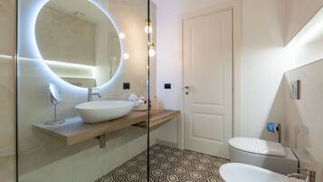 A modern bathroom with a round mirror, a wooden vanity, a freestanding bathtub, and patterned floor tiles.