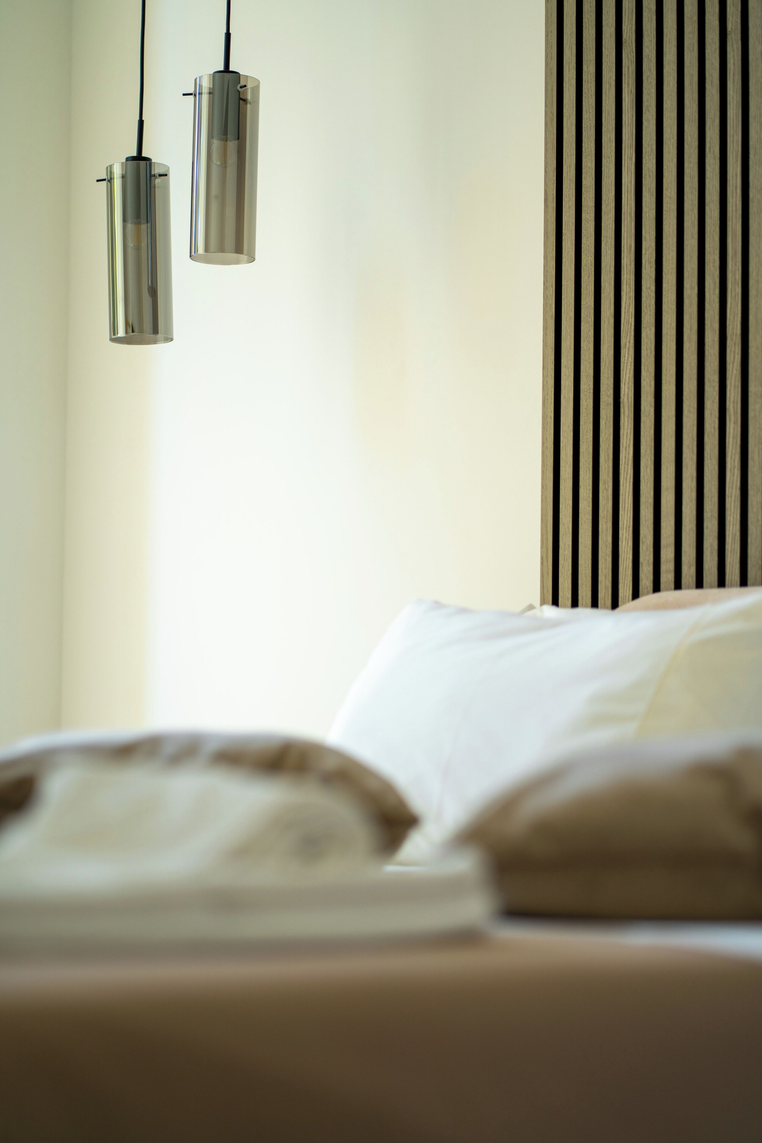 A bedroom with a bed, pillows, and two hanging pendant lights.