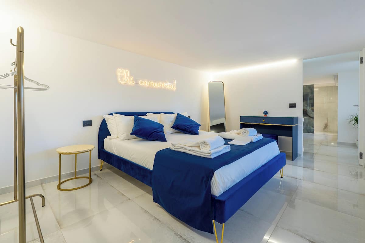 A modern bedroom with a bed, a bedside table, a mirror, and a hanging coat rack.