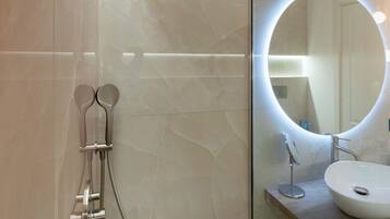 Un baño moderno con ducha envuelta en vidrio, un espejo redondo con iluminación indirecta y una encimera de madera con lavamanos.