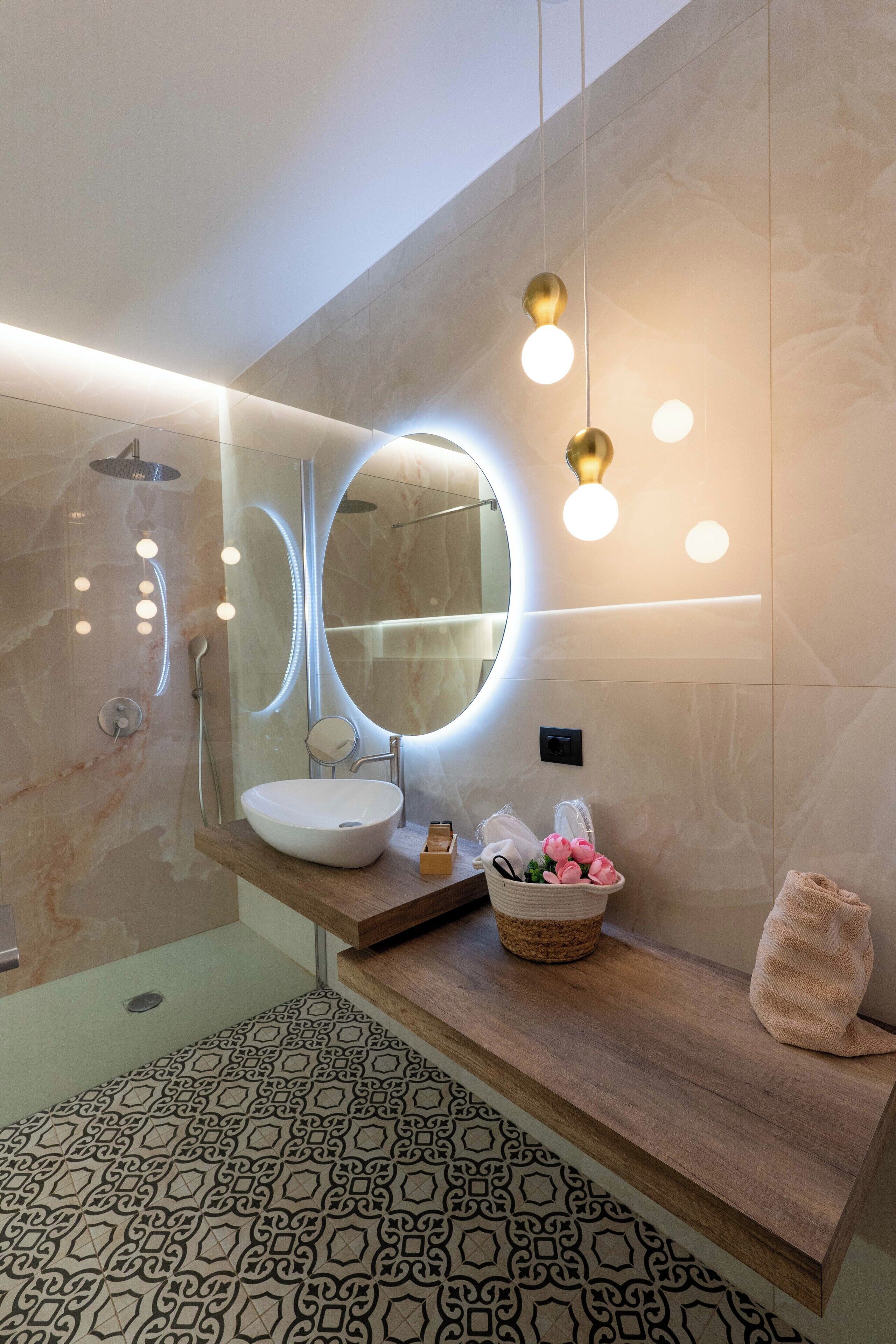 A modern bathroom with a large round mirror, a sink, and a shower.