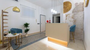 Een moderne hotel lobby met een receptiebalie, een zithoek en een trap.
