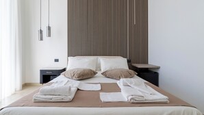 Een netjes opgemaakt bed met een bruine deken, twee kussens en opgevouwen handdoeken. Twee nachtkastjes met lampen, een houten paneel aan de muur, en een raam met gordijnen.