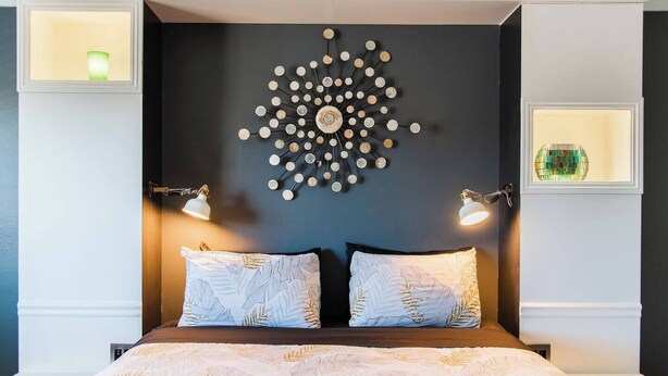 A bedroom with a dark headboard, two bedside lamps, a decorative wall piece, and a bed with patterned bedding. - "Sleepover" Hotel Suite with AC/Heating & Indoor Jetted Tub (Big Bear Lake)