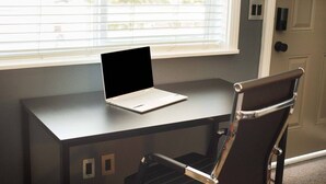 A workspace with a laptop on a dark desk, a chair, and a window with blinds. - "Sleepover" Hotel Suite with AC/Heating & Indoor Jetted Tub (Big Bear Lake)