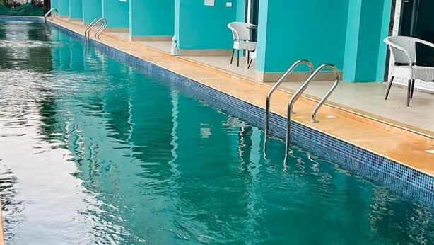A swimming pool adjacent to a building with teal walls and windows. - Ravissant Hotel Mandrem (Mandrem)