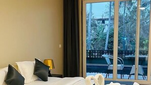 A well-lit bedroom with a large bed, a nightstand, and a view of an outdoor area with chairs and tables. - Ravissant Hotel Mandrem (Mandrem)