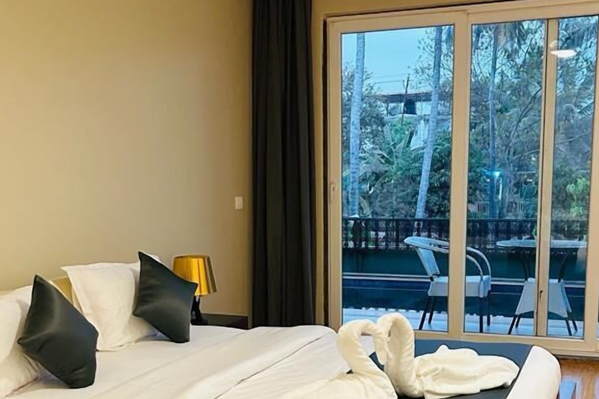 Een goed verlichte slaapkamer met een groot bed, een nachtkastje en uitzicht op een buitenruimte met stoelen en tafels.