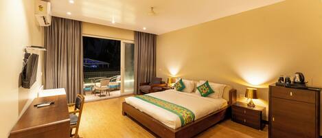 A hotel room with a large bed, a desk, a wardrobe, and a balcony with a pool view.