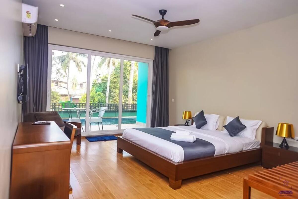 A modern hotel room with a large bed, a desk, and a view of a pool and palm trees.